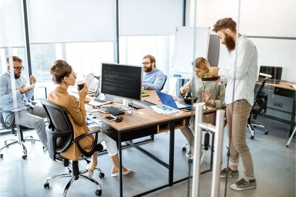 The Office Workplace Comedy Scene Group of coworkers chatting and eating lunch together at their desks in a modern open-plan office reminiscent of The Office TV show workplace comedy setting
