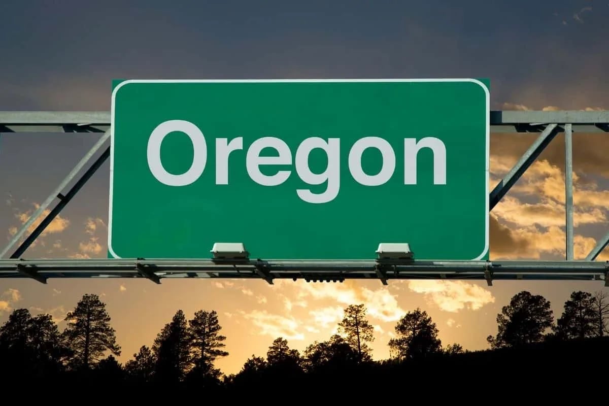 Scenic Oregon highway landscape at sunset with green road sign and silhouetted trees, representing popular filming locations for movies filmed in Oregon
