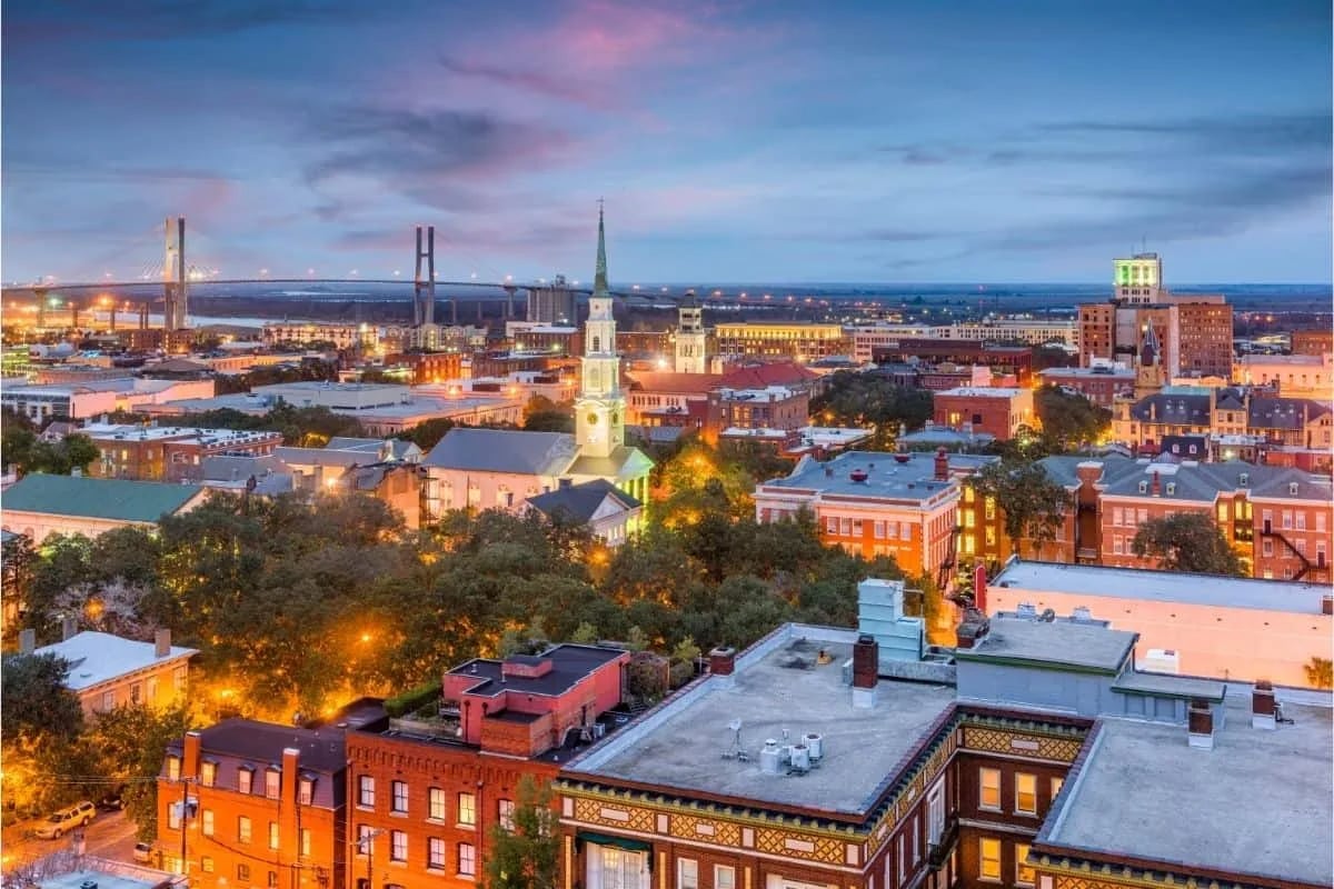 Evening panoramic view of historic downtown Savannah Georgia featuring iconic church steeples and vibrant city lights used as filming locations for popular movies