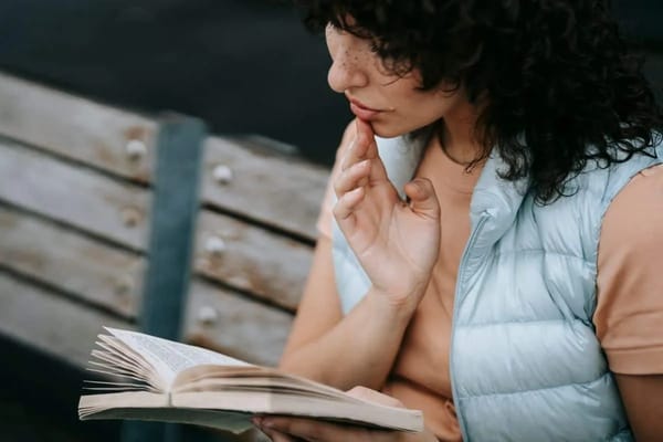 Close-up of a woman reading a book, reflecting while seated on a park bench, enjoying a peaceful outdoor moment.