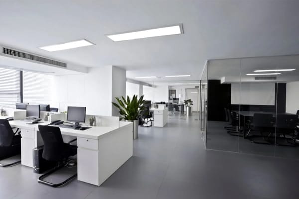 Modern open-plan office workspace with white desks, black chairs, computer monitors, and a glass-walled conference room reminiscent of settings from TV shows like The Office