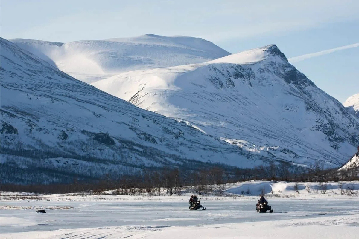 Snow-covered mountains with snowmobiles riding across icy terrain, winter outdoor activity in Norway.