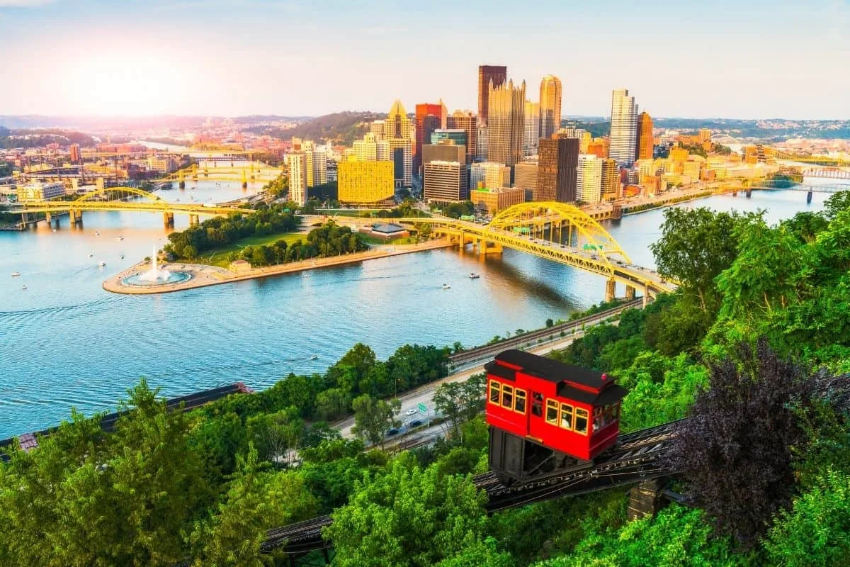 Historic funicular on lush hill with city skyline and river in background.