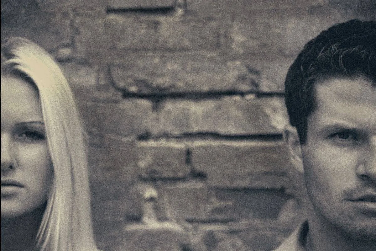 Close-up of a man and woman with intense expressions against a brick wall background.