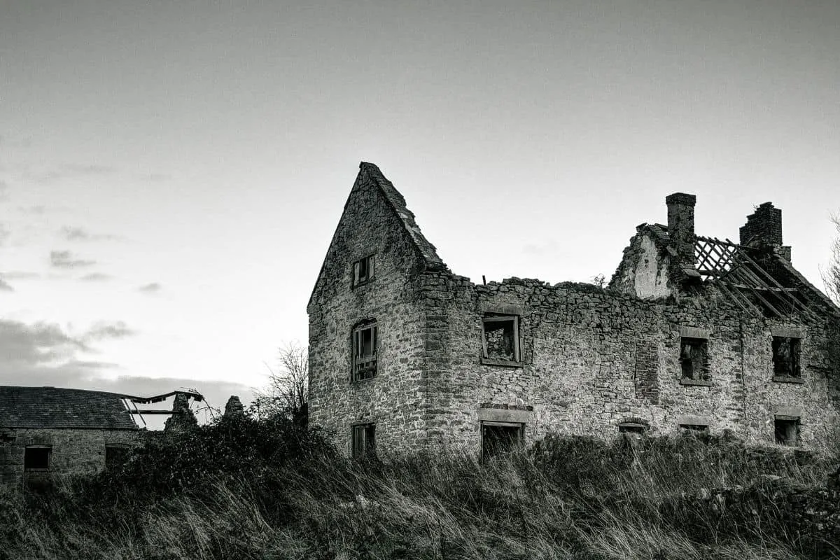 Haunted, abandoned house in black and white with broken windows and damaged roof.