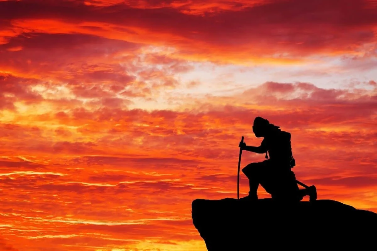 Silhouette of a hiker with a walking stick on a rocky cliff at sunset.
