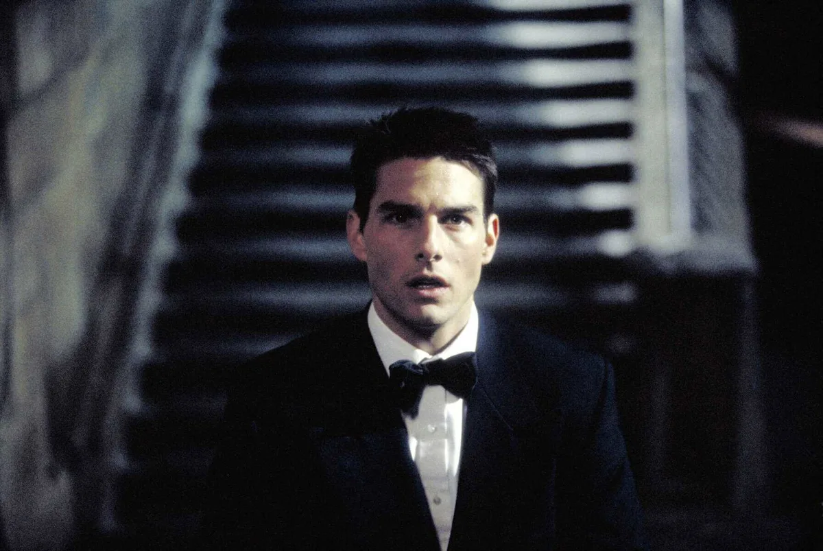 Young man in tuxedo with short dark hair looking shocked or surprised in a cinematic scene.
