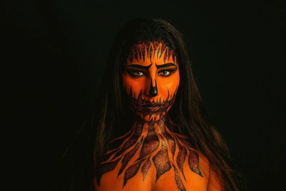 Vibrant orange and black Halloween face makeup with pumpkin and flame patterns.
