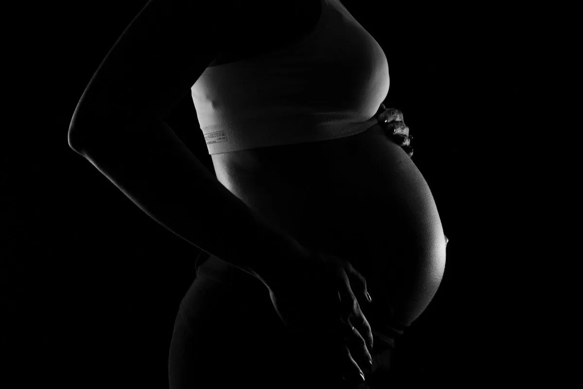 Dark silhouette of pregnant woman with visible belly and hand on hips.