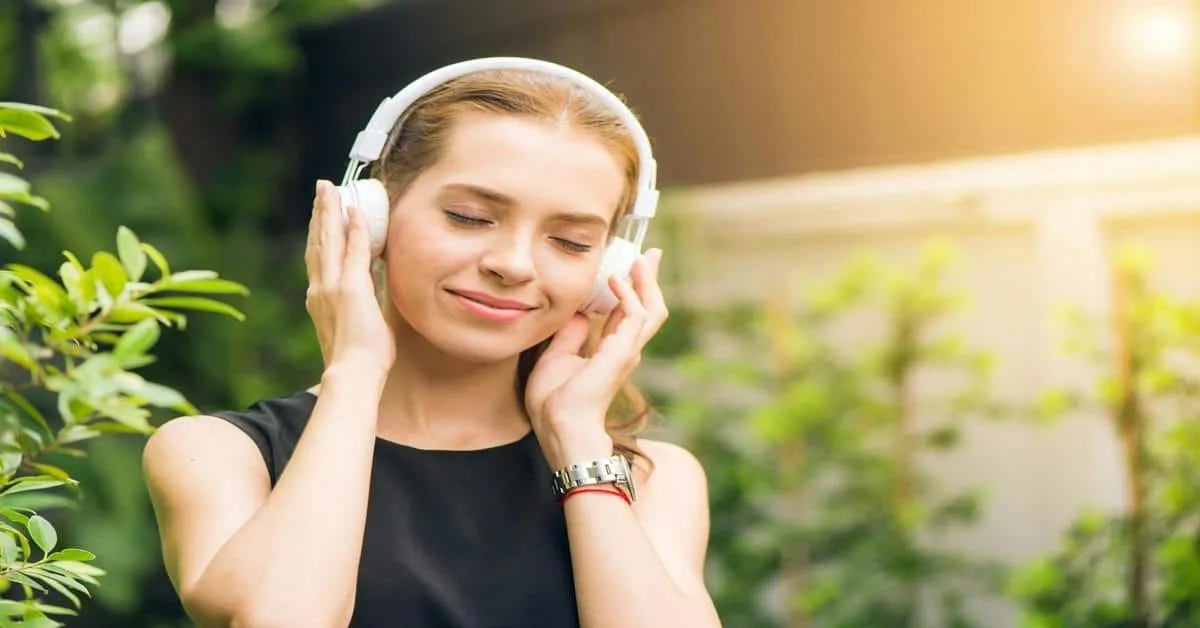 Young woman with headphones listening to music outdoors, enjoying a peaceful moment.