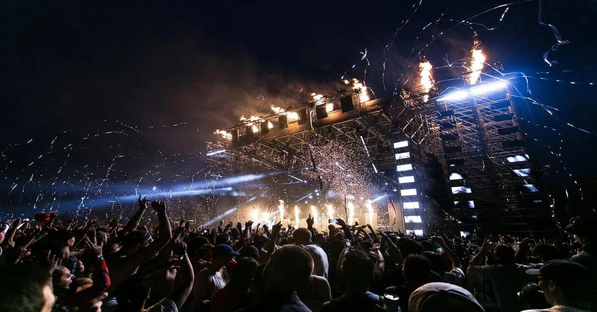 Vibrant stage with pyrotechnics and energetic crowd at a nighttime music event.