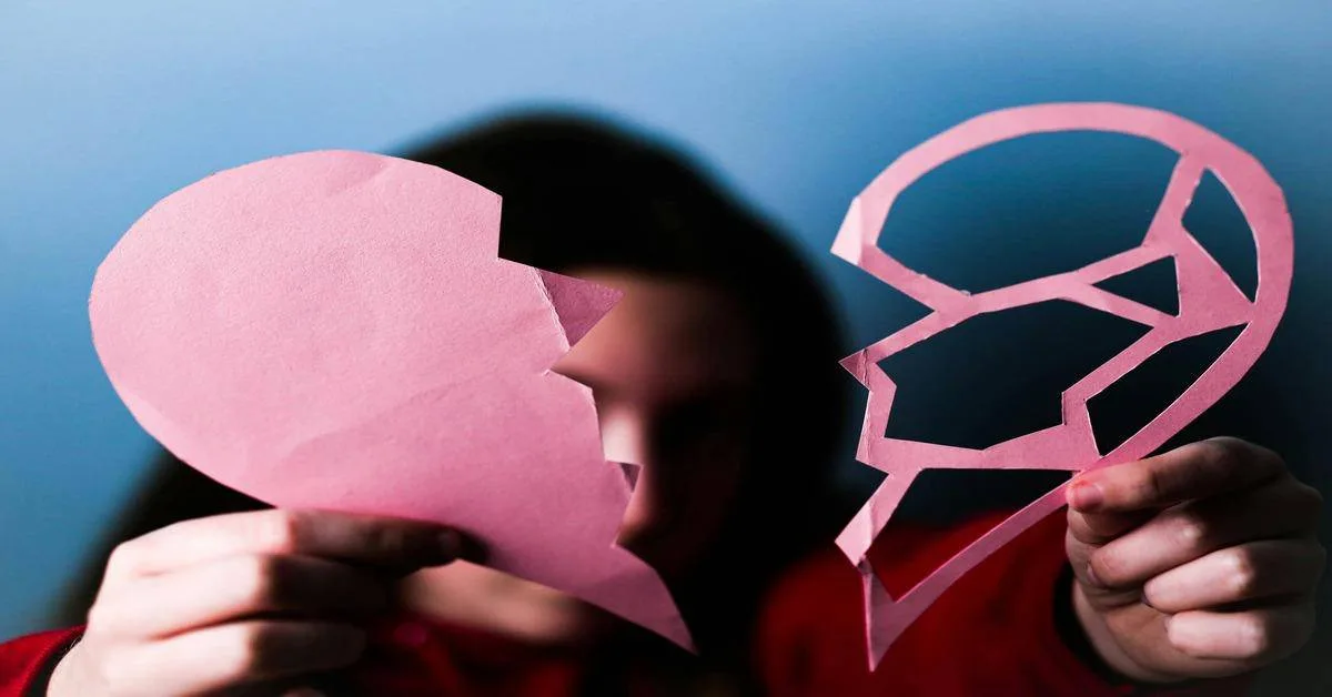 Heart broken paper cutout with person holding it, symbolizing heartbreak or emotional pain.