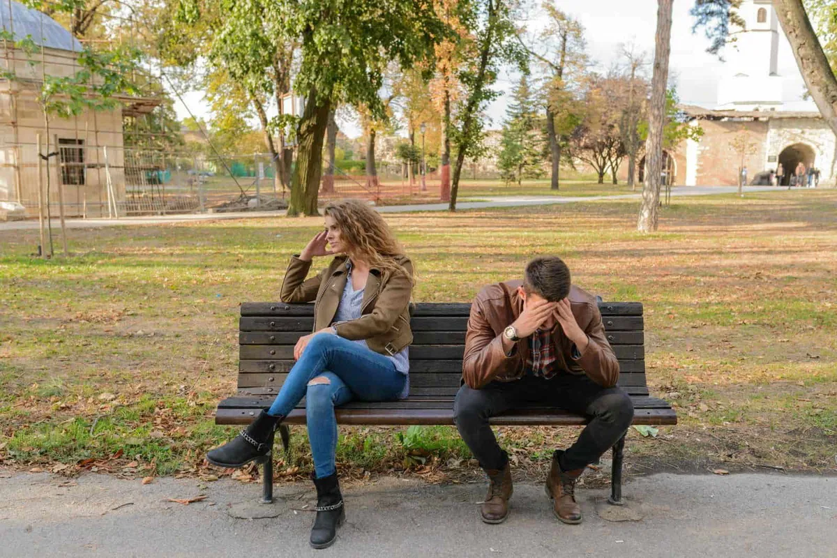 Young woman and man sitting on park bench, appearing upset and stressed.