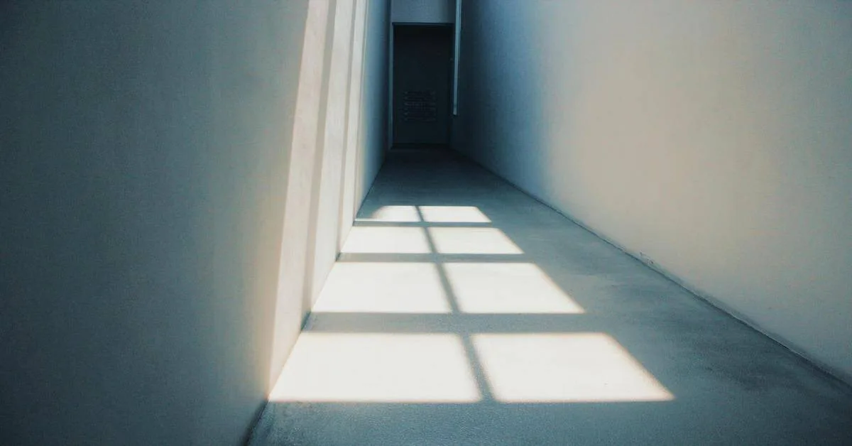 Modern interior corridor with sharp sunlight shadows and clean minimalist design.