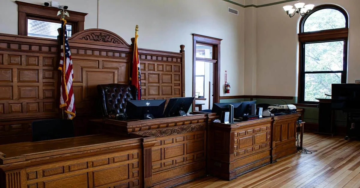 Courtroom with wooden judge’s bench, American flag, and legal equipment, bright natural light, and classic courtroom design.