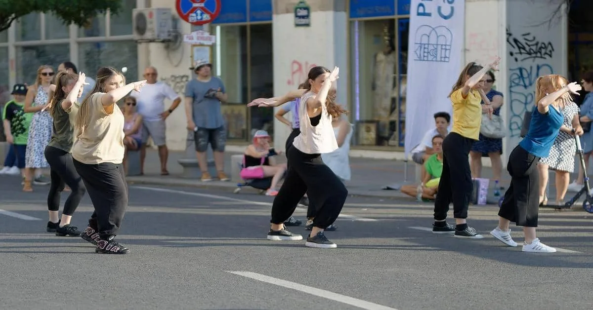 Energetic women performing dance outdoors on busy city street, spectators watching.