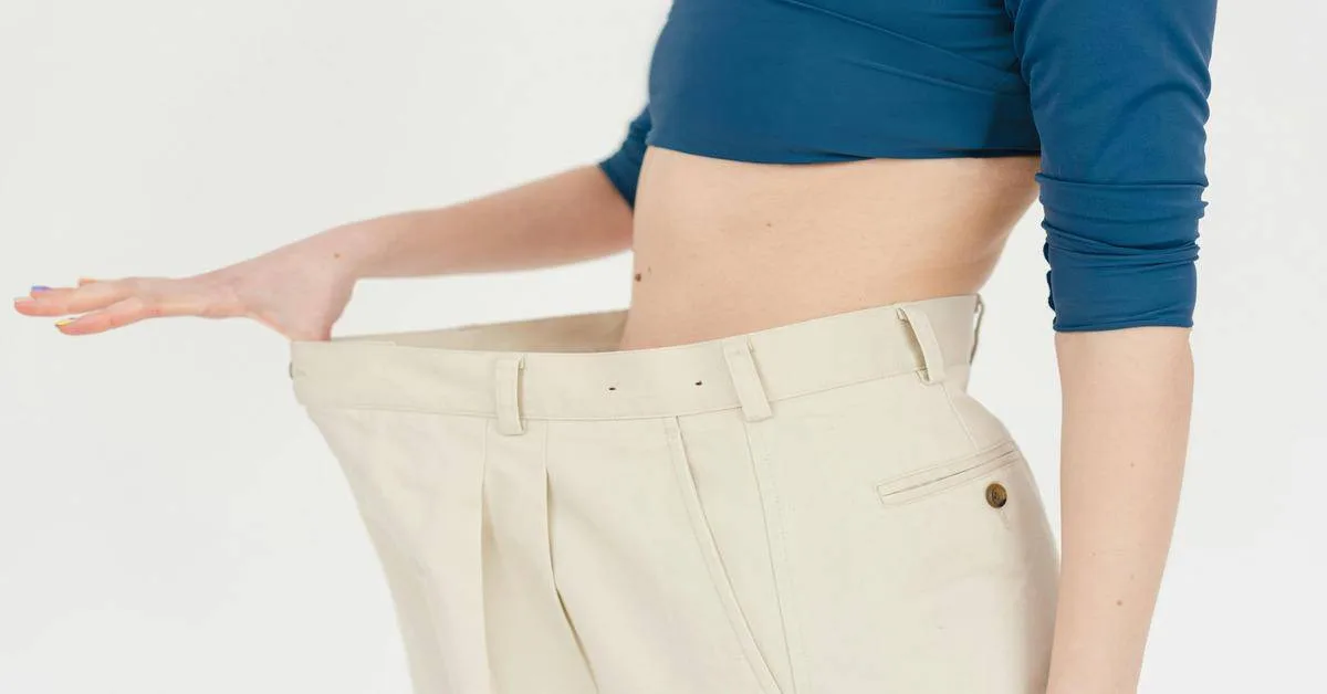 Close-up of a woman measuring her waist with oversized clothing, emphasizing weight loss and body transformation.