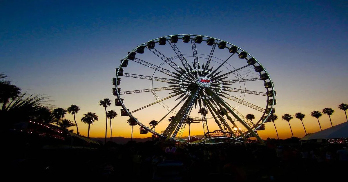 Brightly lit Ferris wheel during sunset with silhouetted palm trees and a lively outdoor setting.