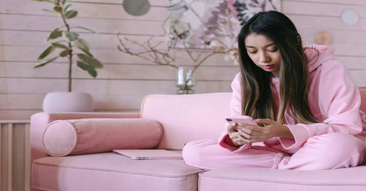 Alt text: Woman in pink loungewear using smartphone on pink sofa, cozy home setting.