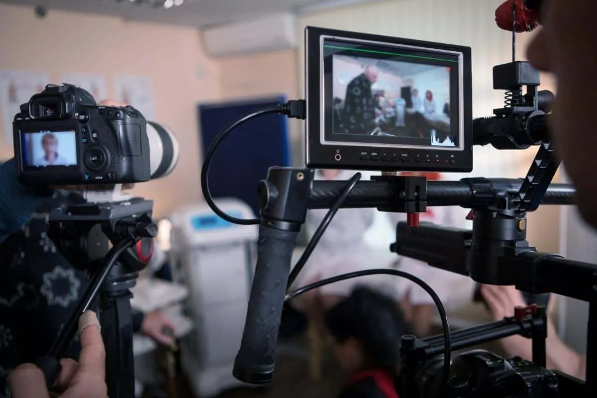 Behind the scenes TV comedy production setup with DSLR camera and external monitor on a gimbal rig filming a scene reminiscent of mockumentary shows like Arrested Development and The Office