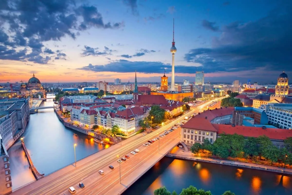 Aerial dusk view of Berlin skyline featuring the iconic Fernsehturm TV Tower and illuminated bridges over the Spree River, representing the cinematic backdrop for movies about Berlin