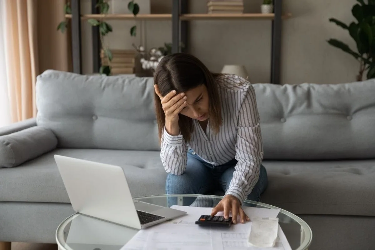 Overwhelmed woman sitting on sofa with laptop and calculator illustrating depression symptoms and mental health struggles