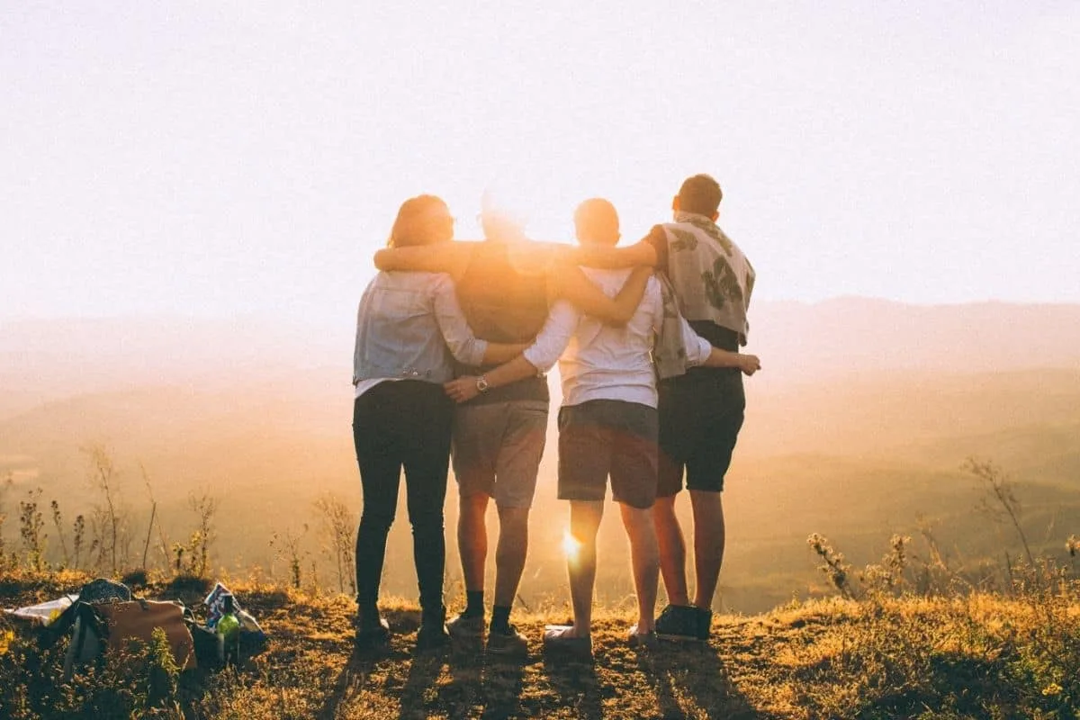 Group of friends embracing and smiling during a golden sunset in nature highlighting the bond in movies about friendship