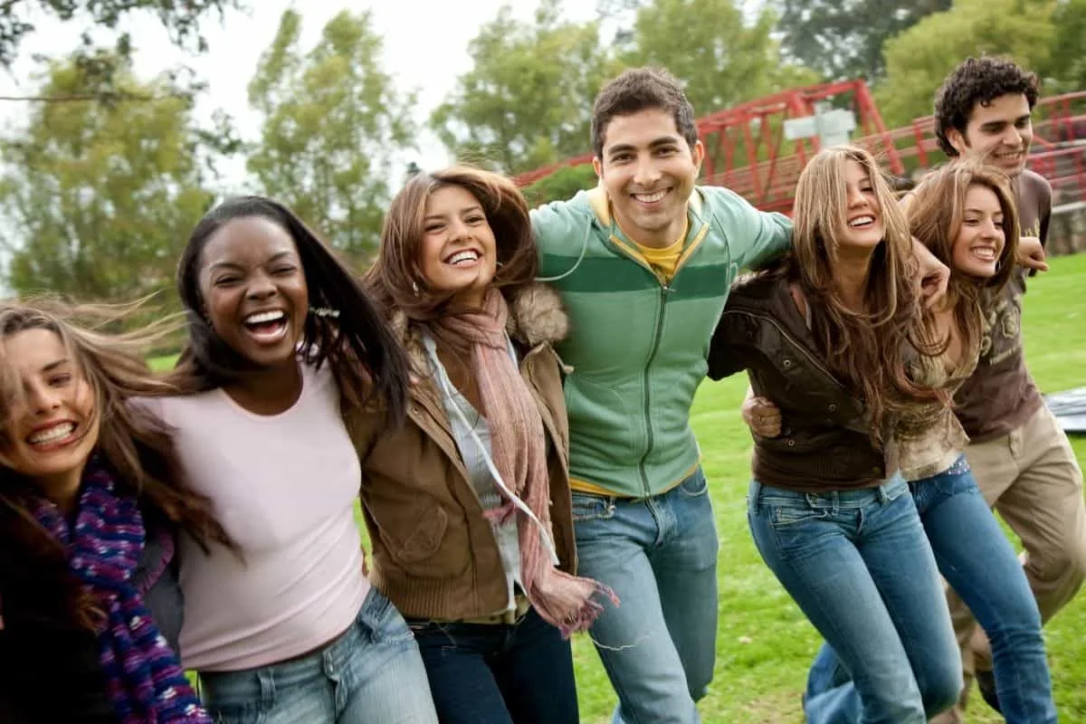 Group of diverse teenage friends laughing and walking together outdoors in a park setting reminiscent of teen drama TV shows like Ginny and Georgia and Riverdale