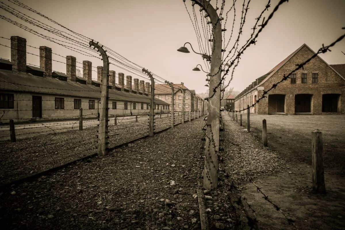 Black and white scene from Schindler's List movie summary showing a desolate WWII concentration camp with barbed wire fences and barracks representing the plight of the Jewish workforce under Oskar Schindler